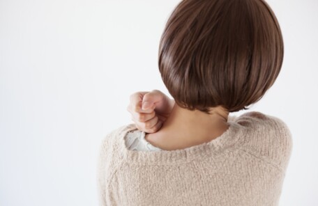 肩こりを気にして首肩に手を当てる女性の後ろ姿