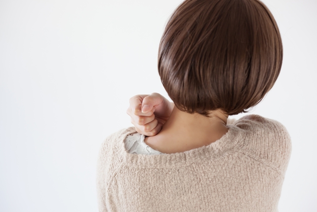 肩こりを気にして首肩に手を当てる女性の後ろ姿