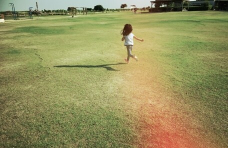 風を感じながら草原を走る子どもの後ろ姿