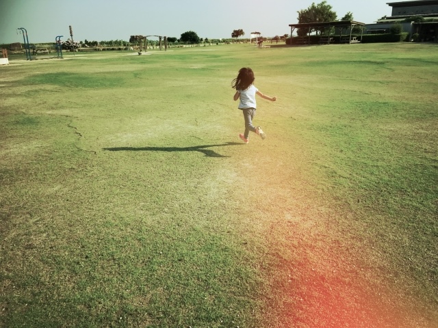 風を感じながら草原を走る子どもの後ろ姿
