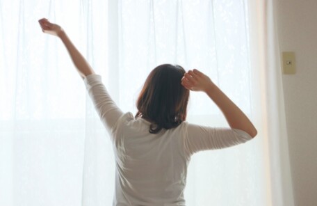 自宅で朝の光の中、無理のない伸びをして体を整えるイメージ